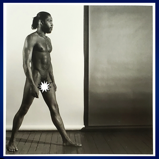 A black and white art photograph of a nude black gay male figure standing in profile against a studio backdrop, with a white starburst censor block over the genital area. Sold in The Pink Rocket New Orleans gay owned small business.