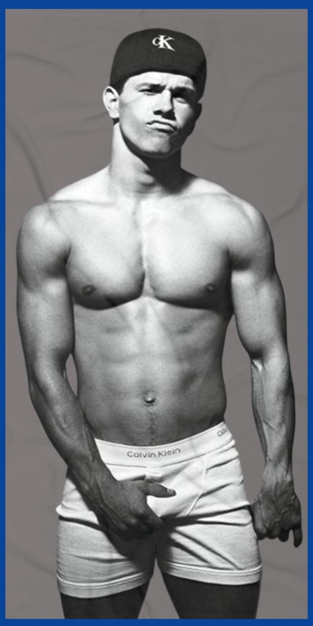 A black and white fashion photograph of Marky Mark wearing a black Calvin Klein cap and white Calvin Klein briefs on a premium beach towel by The Pink Rocket New Orleans a fay owned gift shop.