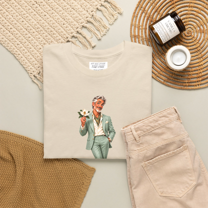 A gfolded cream colored short-sleeve t-shirt with a graphic of a gay man in a light green suit holding a flower, with the text "Flawlessly Southern, darlin'" printed below in brown letters. Designed and for sale in The Pink Rocket New Orleans gay gift shop.