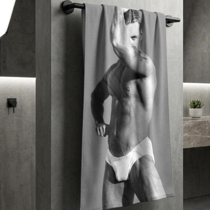 A custom beacjh towel hanging to dry in a modern bathroom with a photo of a hunky gay man in a bathing suit. Sexy and ready for the beach. For sale in The Pink Rocket New Orleans gay owned gift shop.
