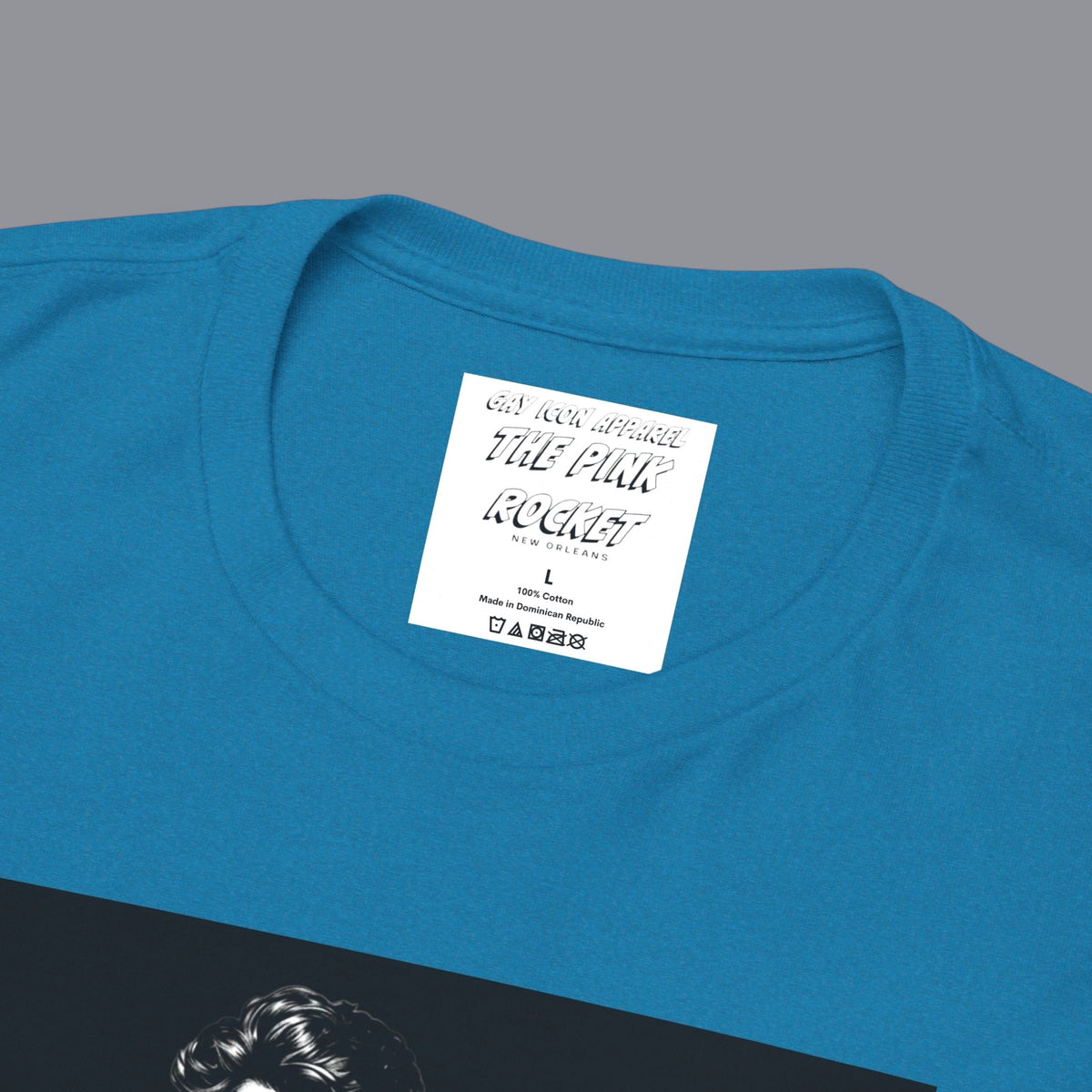A closeup of a teal blue short-sleeve t-shirt with a graphic print of a gay muscular shirtless man wearing blue pants, with the text 'GYM-MAXXING' printed below the graphic. Designed and for sale in The Pink Rocket New Orleans gay gift shop.