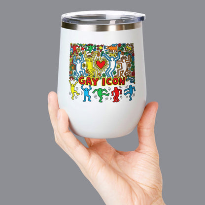 A hand holding a white 12oz. insulated stemless wine tumbler with a clear lid. The tumbler features a colorful graphic of dancing figures and the words 'GAY ICON' in red, yellow, and blue. Designed and sold in The Pink Rocket New Orleans gay gift shop.