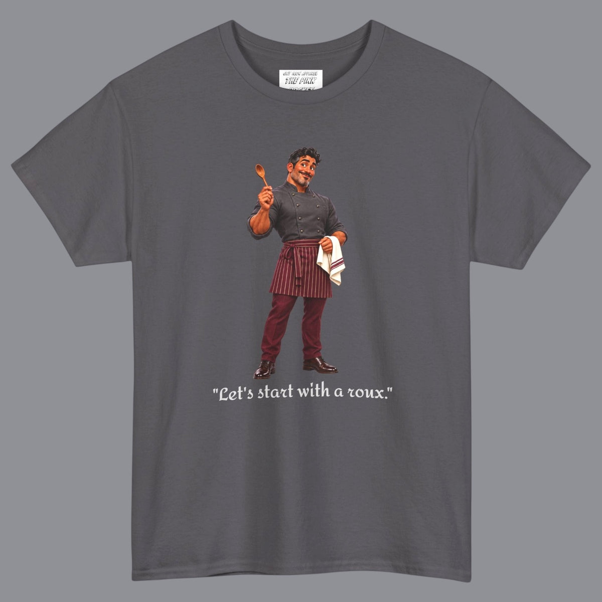 A gray short-sleeve t-shirt with a graphic of a gay male chef  in a holding a wooden spoon with the text "Let's Start With A Roux" printed below in off white letters. Designed and for sale in The Pink Rocket New Orleans gay gift shop.