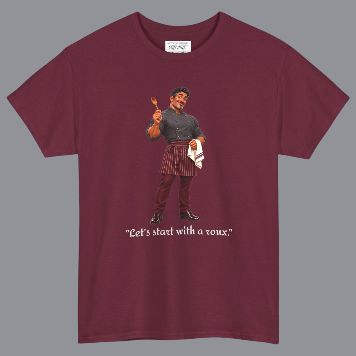 A wine colored short-sleeve t-shirt with a graphic of a gay male chef  in a holding a wooden spoon with the text "Let's Start With A Roux" printed below in off white letters. Designed and for sale in The Pink Rocket New Orleans gay gift shop.