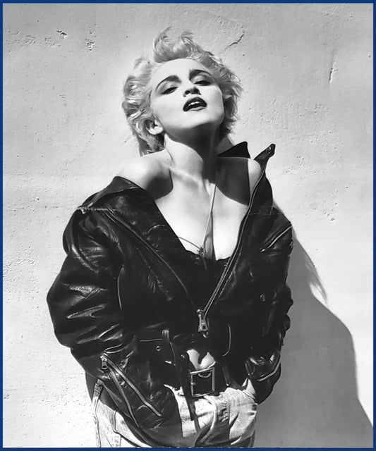 Black and white fashion photograph of Madonna in her True Blue era wearing an open black leather jacket, looking upward against a textured wall. Sold in The Pink Rocket New Orleans gay gift shop.