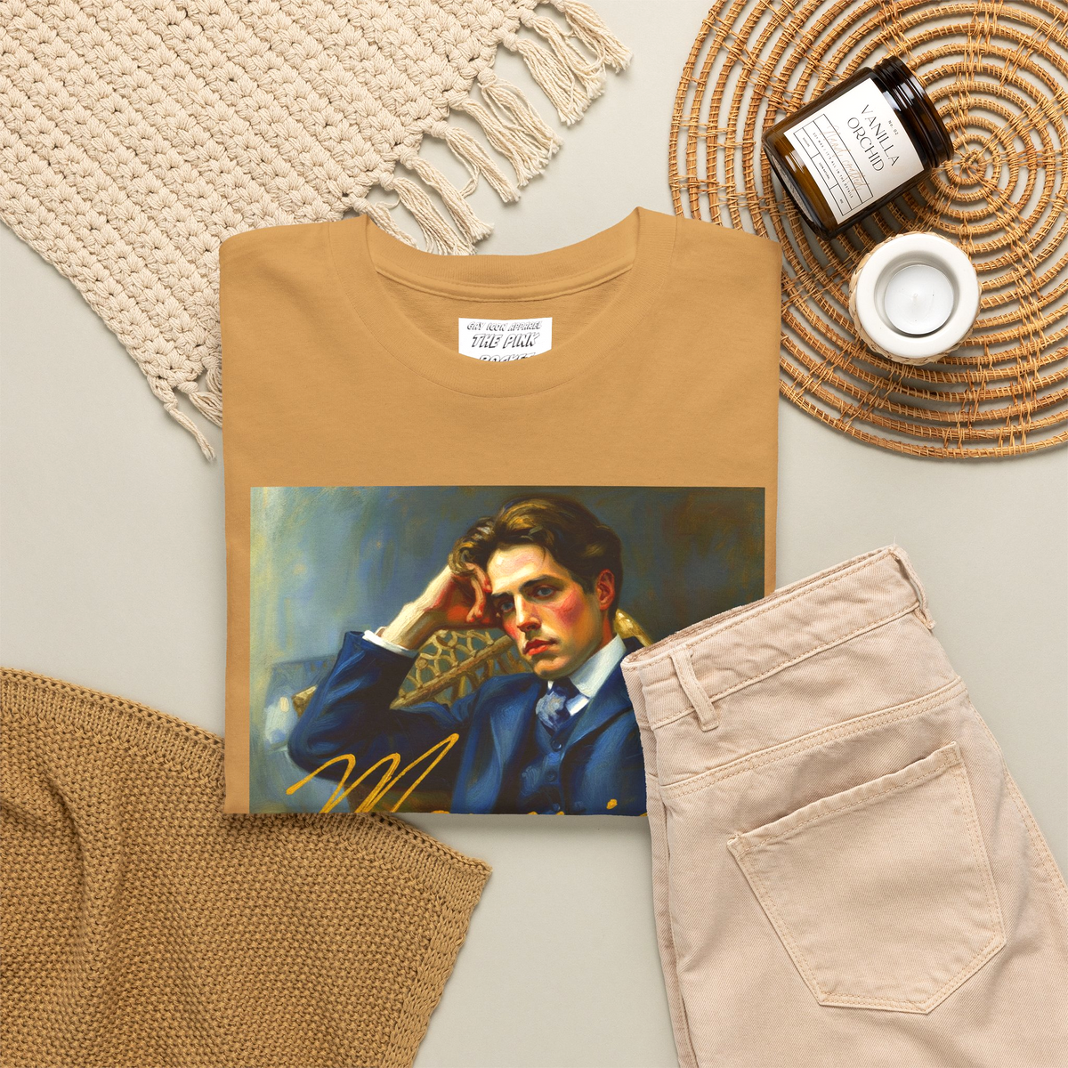 A folded-gold bronze short-sleeve t-shirt with a rectangular graphic print of the gay 80's film Maurice on the chest depicting a portrait of a man in a blue suit and the name 'Maurice' in gold script. Designed and available in The Pink Rocket New Orleans gay gift shop.
