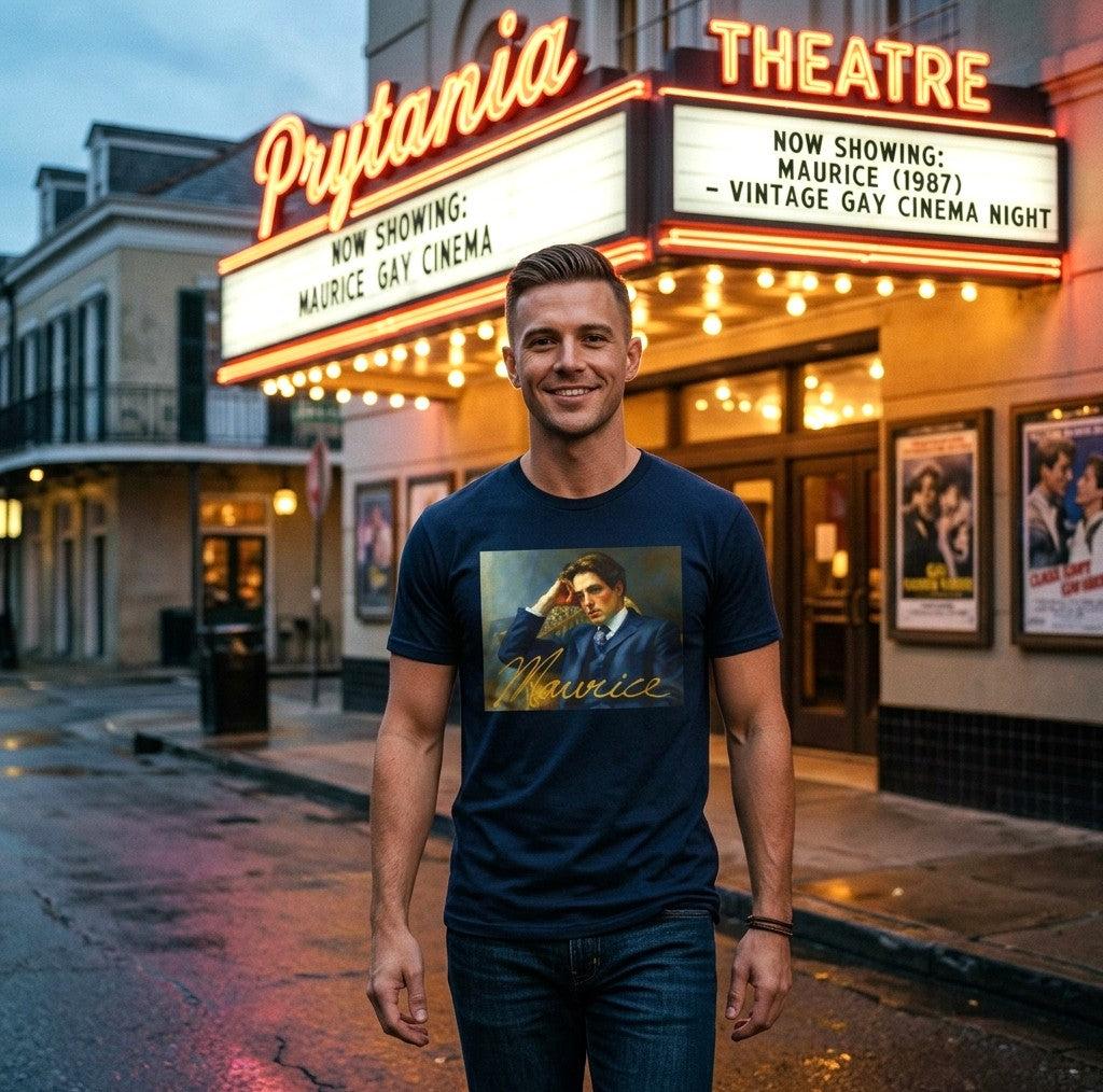 A hunky gay man stands in front of a lit movie theater marquee at dusk, wearing a navy graphic T-shirt with a printed portrait and the word 'Maurice' from the 80's film in gold script, paired with dark jeans. Designed and available in The Pink Rocket New Orleans gay owned gift shop.
