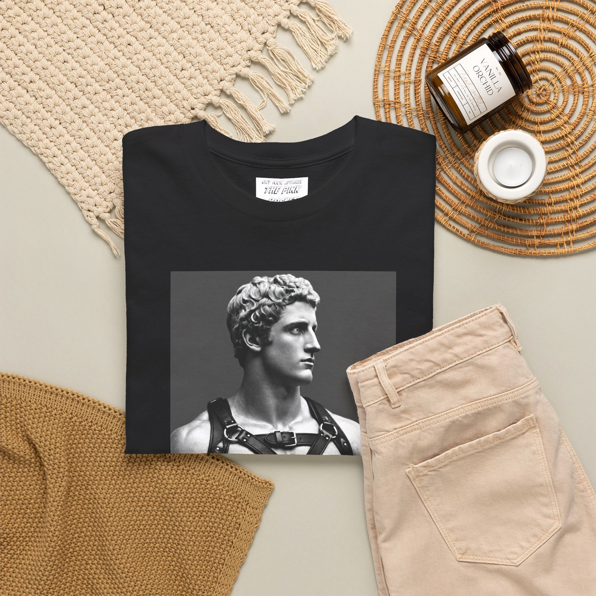 A folded black crewneck t-shirt featuring a black-and-white graphic print of a muscular classical Apollo statue wearing a harness. Designed and sold in The Pink Rocket New Orleans gay owned gift shop.
