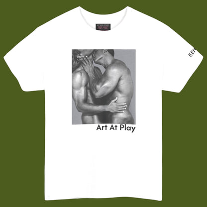 A white crewneck t-shirt featuring a black and white graphic print of a nude gay male couple embracing and kissing, with the text 'Art At Play' printed below the image. Designed and for sale in The Pink Rocket ew Olreans gay gift shop.