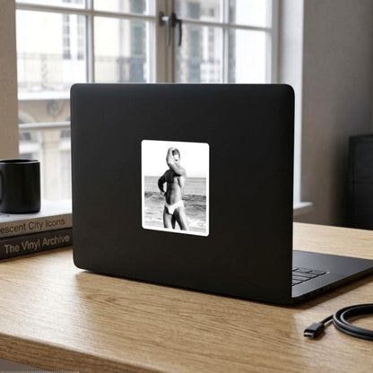 A black and white photograph of a sexy hunky muscular man posing on a beach, wearing white briefs. The image is presented with a white border. For sale in The Pink Rocket New Orleans gay gift shop.