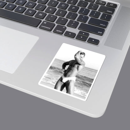 A black and white photograph of a sexy hunky muscular gay man posing on a beach, wearing white briefs. The image is presented with a gray border. For sale in The Pink Rocket New Orleans gay gift shop.